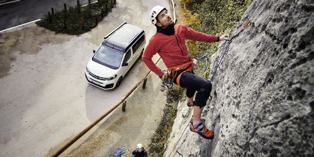 Ein Mann klettert gesichert eine Felswand hoch, unten ist ein Off Camper zu sehen