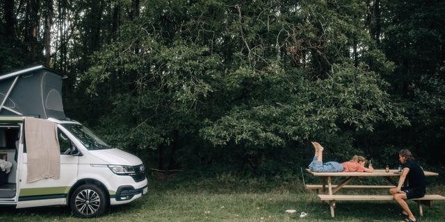 Vater und Tochter chillen an Holztisch beim Camping in Natur