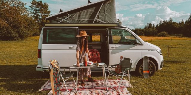 Eine Frau deckt vor einem offenen CamperBoys Camper, der auf einer Wiese steht, den Campingtisch.