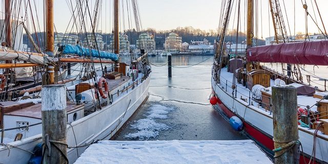 Snow on a dock with two boats. The water is halfway frozen. 