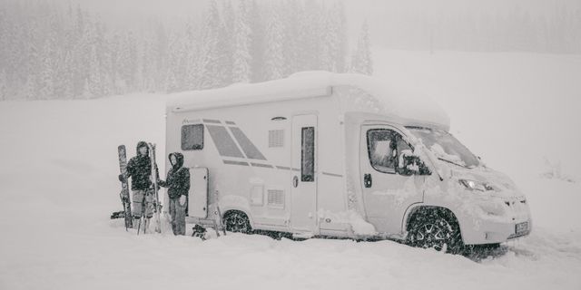 2 Personen mit Skiern in den Händen stehen im Schnee vor einem ganz verschneiten Off Wohnmobil