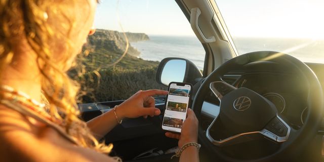 A woman inside a camper van is using the CamperBoys route service on her phone.
