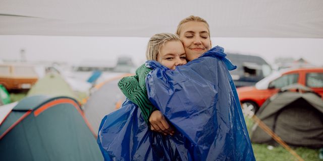 Zwei Frauen umarmen sich auf einem Festivalgelände, um sie herum sind Autos und Zelte zu sehen. Hier findest du unsere Festival Packliste.