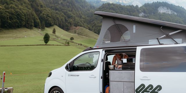 Schweiz Urlaub mit dem Camper: Frau steht in Off Camper vor Wiesen und Bergen