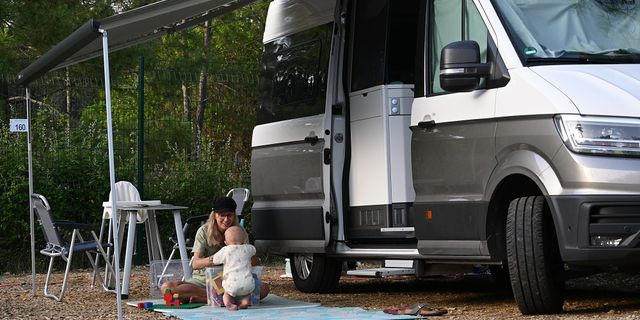 Eine Frau und ein Baby sitzen vor einem VW Grand California Van am Boden.