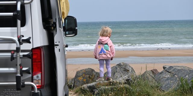 A little child standing at the beach. Next to her is a parked CamperBoys van.