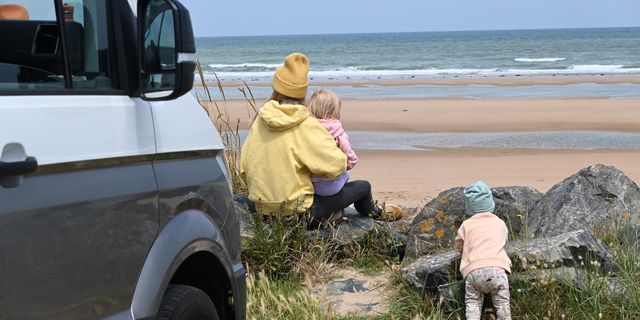 A mother with two little children at the beach and a CamperBoys van next to them 