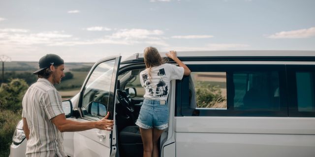 Ein Mädchen lehnt in der Türöffnung eines geparkten VW Ocean Campers, ihr Vater hat die Hand an der Tür und scheint diese offen zu halten.