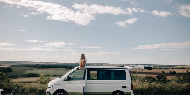 Eine Frau sitzt auf dem Dach eines auf einer Wiese geparkten VW California Ocean Vans. 