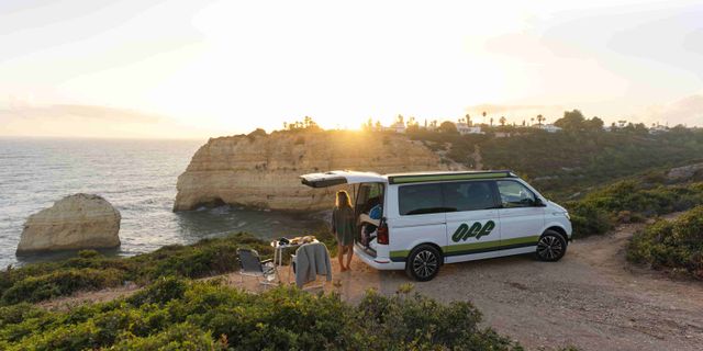 Junge Frau in Portugal an der Kueste neben Off Camper bei Sonnenuntergang