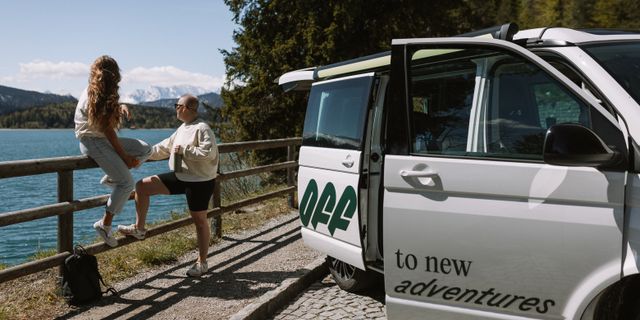 Zwei Freundinnen sitzen beim Camping an einem Zaun neben einem Off Camper