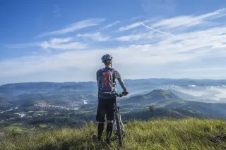 Mann mit Fahrradhelm bewundert die Aussicht ins bergige Tal in Österreich auf seinem Fahrradurlaub mit dem Mountainbike von einer grünen Wiese aus