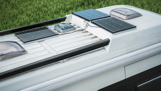 Wohnmobil Stromversorgung mit Solaranlage: Das Dach eines Campers mit Solarpanelen, der auf der Wiese steht.