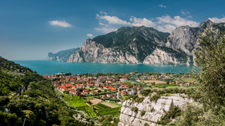 Schöne Orte in Italien: Blick von oben auf eine Stadt am Gardasee mit türkisblauem Wasser und die Berge im Hintergrund.