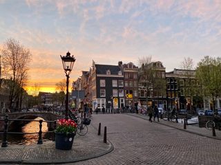 Eine Brücke in Amsterdam mit rosa Wolken und Sonnenuntergang im Hintergrund, vor der Kulisse von Grachten und Fachwerkhäusern