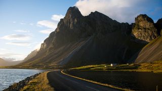 Ein leerer Straßenabschnitt auf der Island Rundreise in 10 Tagen direkt am Meer mit imposanten Bergen an der Straßenseite