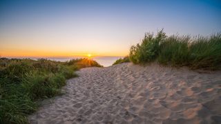 Ein sandiger Weg in den Dünen zum Meer, über dem gerade die Sonne untergeht in Zeeland in den Niederlanden