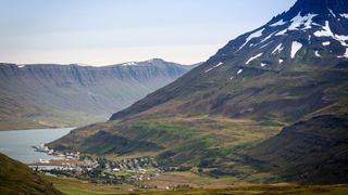 Die Island Rundreise 10 Tage führt auch an den Ostfjorden vorbei: Hier sieht man einen Fjord neben einem grünen Bergrücken, der teilweise noch mit Schnee bedeckt ist 
