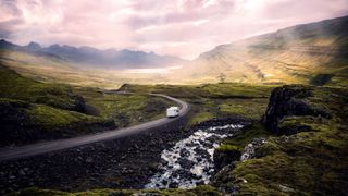 Camping Island: Ein Campervan auf einer Straße in grüner Berglandschaft auf Island