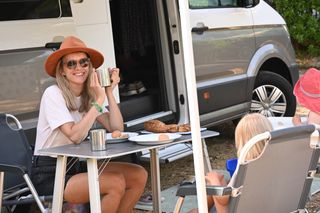 Familienurlaub mit dem Camper in Holland am Meer: Eine Mutter mit rotem Hut sitzt am Tisch vor dem Camper gegenüber ihrer kleinen Kinder auf einem Campingplatz in Holland am Meer