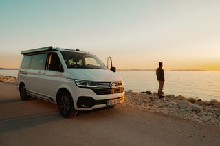 Man standing next to camper van and looking at the sea at sunset