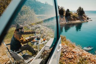 Man having breakfast next to a camper van at the lake