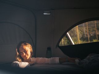 Eine Frau steht beim Alpsee Camping in einem Camper und baut das Dachbett auf.