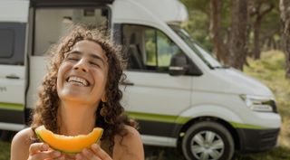 Frau isst vor dem Camper eine Melone