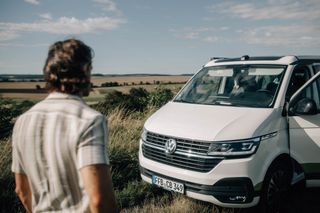 Ein Mann schaut auf seinen Off Camper VW Bus, der am Straßenrand neben einem Feld parkt