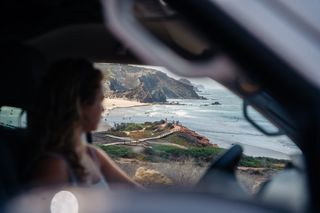 Eine Frau fährt einen California Beach Van und schaut aus dem Fenster, man sieht die portugiesische Algarve Küste und das Meer. Karibik in Europa findet man auch in Portugal.