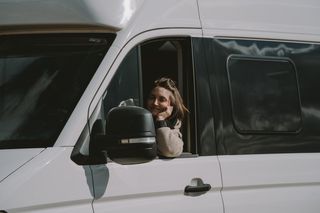 Frau lehnt sich aus Fenster eines fahrenden Campers heraus