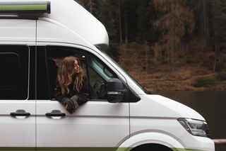 Frau mit wehenden Haaren schaut im Herbst während der Fahrt aus dem Fesnter ihres Campers