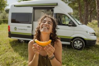 Eine Frau lacht und hält ein Stück Honigmelone in der Hand.