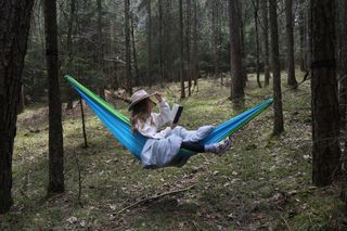 Eine Frau liest in einer Hängematte im Wald.