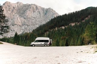 Ein Grand California Van steht beim Camping in Albanien geparkt vor einer Bergkulisse, ein Mann öffnet hinten die Heckklappe.