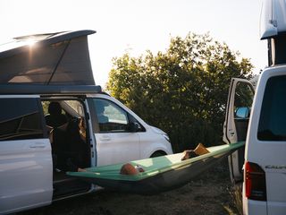 Eine Person liegt beim Camping am Bannwaldsee in einer Hängematte, die zwischen zwei Campern gespannt ist.
