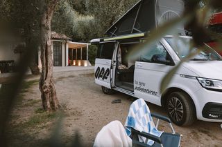 Ein VW California Camper Van steht auf einem Campingplatz am Gardasee mit geöffneter Tür.