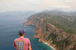 Mann mit buntem Shirt schaut aufs Meer und Berge an der Küste in Korsika