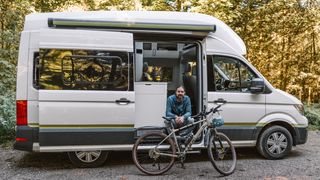 Ein Mann steht mit seinem Campervan auf dem Campingplatz Camping Brugger am Riegsee: vor ihm sein Fahrrad, mit dem er gleich eine Tour beginnt