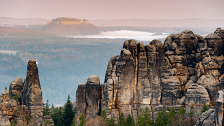 Felsformationen mit Nebelfeldern im Wald und einer Festung im Hintergrund