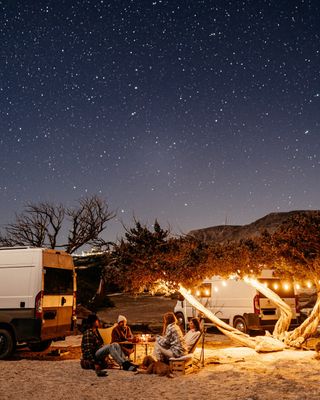Camper sitzen am Lagerfeuer unter einem Sternenhimmel.