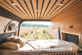 Innenraum des Boho-Van "Lotti": Bett mit Ausblick auf ein sonniges Kornfeld