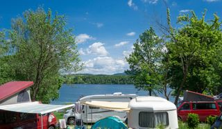 Der Campingplatz Brugger am Riegsee: Camper und Wohnmobile stehen direkt am Ufer des Riegsees zwischen Bäumen
