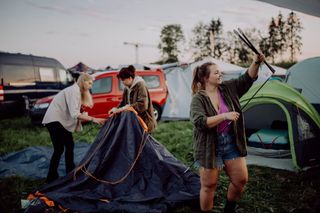Drei Frauen bauen auf einem Festivalgelände ihre Zelte auf.