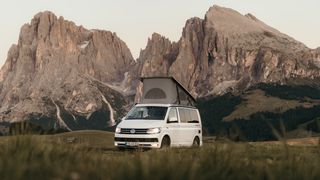 Dolomiten Geheimtipps: Ein Off Camper mit Aufstelldach fährt vor schroffen Bergen in den Dolomiten eine Straße entlang