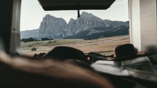 Ein Mann, der die schönsten Orte in Südtirol mit dem Camper erkundet, schaut aus dem Fenster des Campers auf die Berglandschaft, neben ihm liegt ein Hut