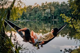 Zwei Frauen liegen bei Sonnenuntergang in einer Hängematte und blicken auf einen See.