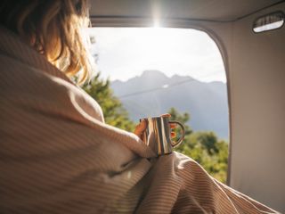 Frau sitzt mit Wärmflasche und Tee im Camper und schaut aus dem Fenster