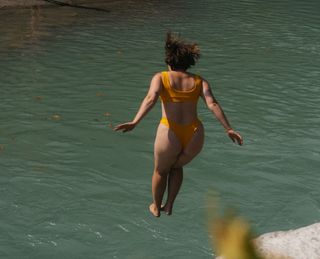 Frau springt von kleinem Fels in türkis blaues Wasser