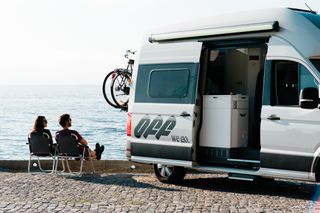 Warme Reiseziele April: Ein Pärchen sitzt in Kroatien neben ihrem Campervan auf Campingstühlen in der Sonne direkt am Meer